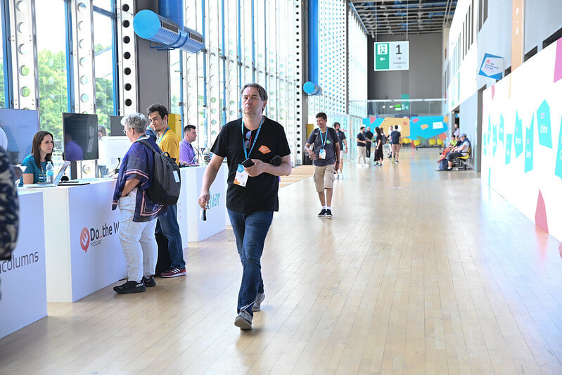 A bustling event hall with attendees walking and interacting at various booths during WordCamp Europe 2024.