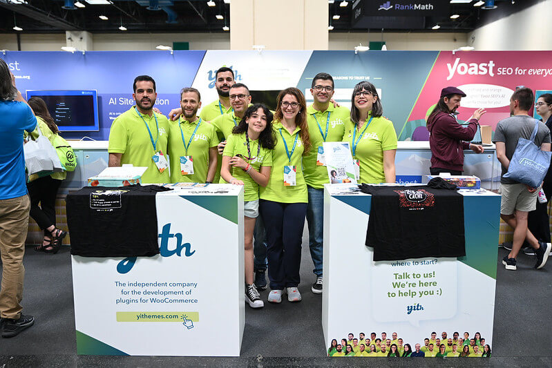 A group of smiling Yith team members posing together at their booth at WordCamp Europe 2024.